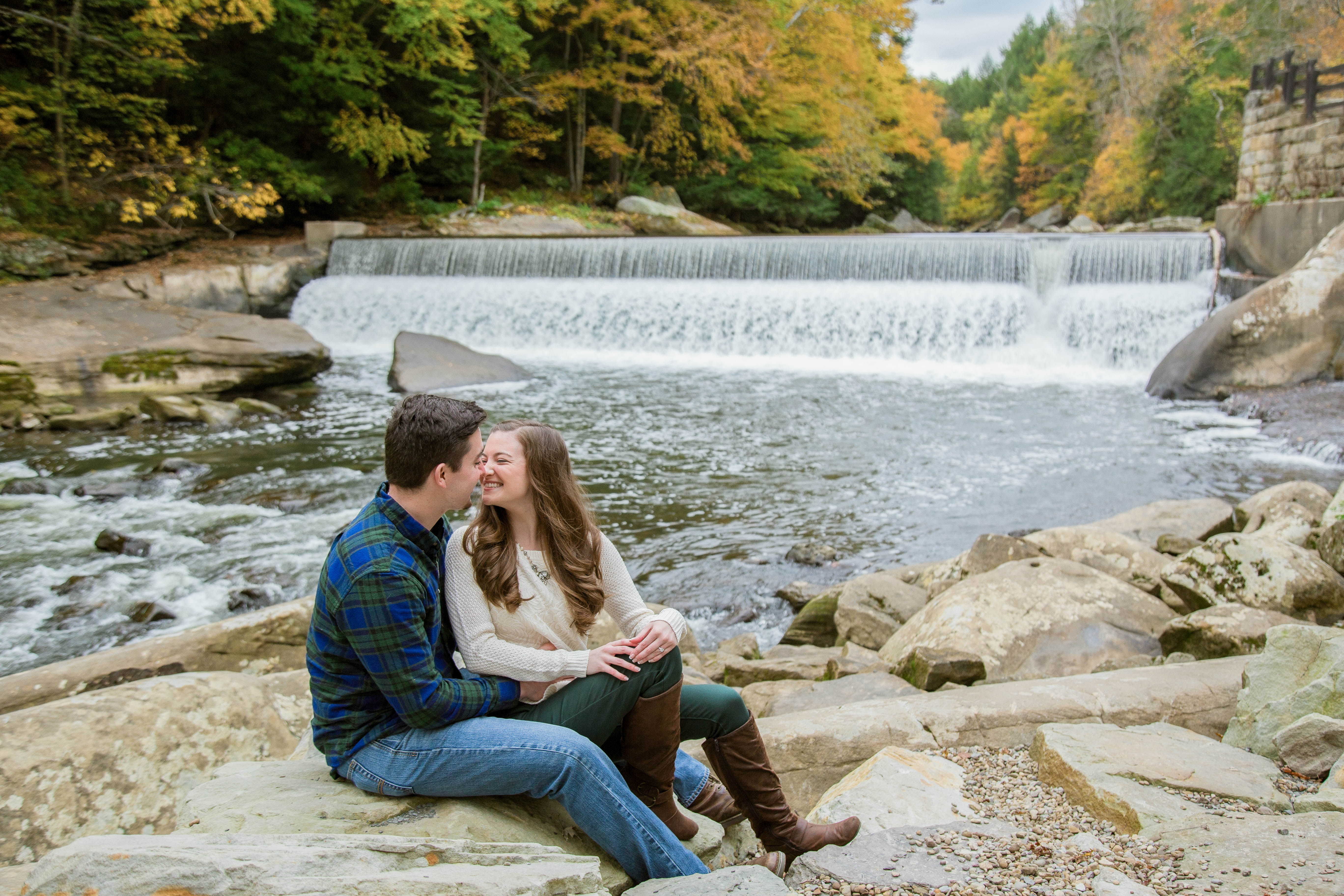 couple snuggles on the rocks in front of the waterfall at the mill in mcconnells mills