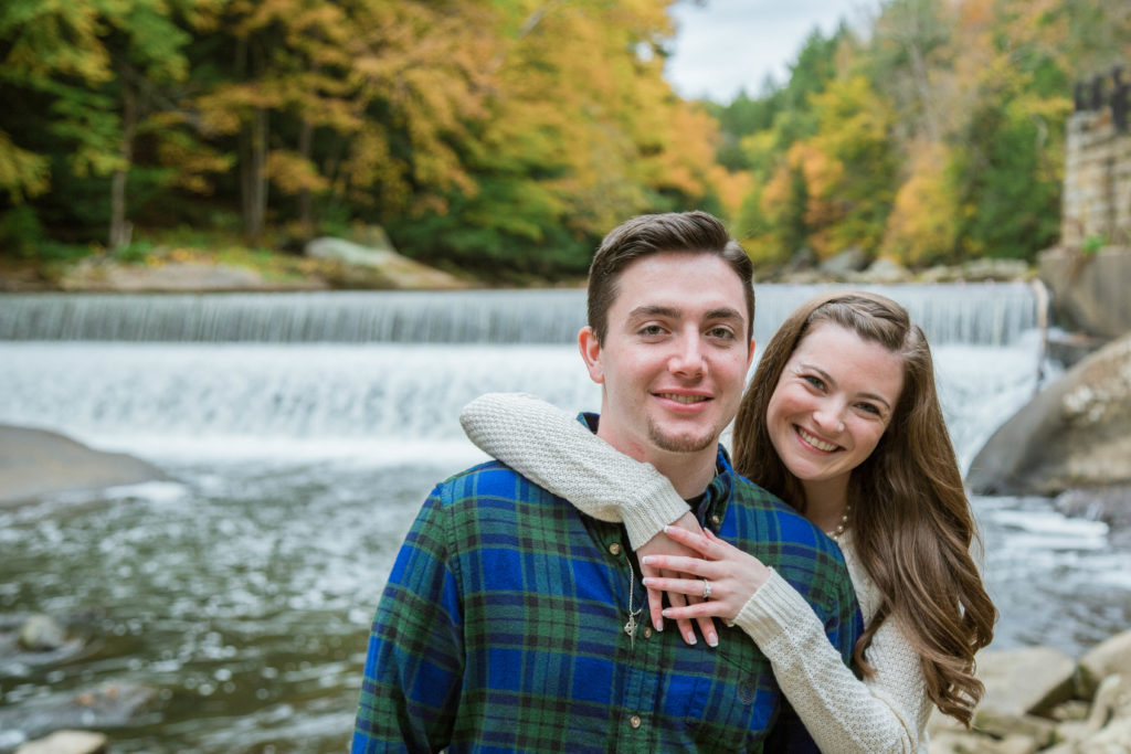 woman hugs man from behind as they stand in front of waterfall