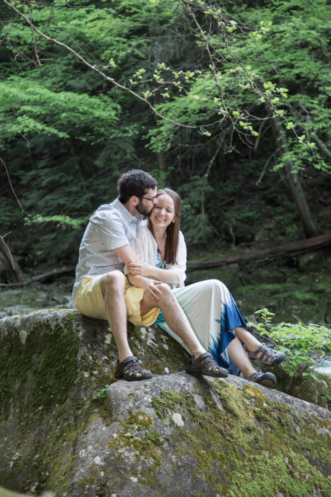engaged couple sits o a rock in mcconnells mills park