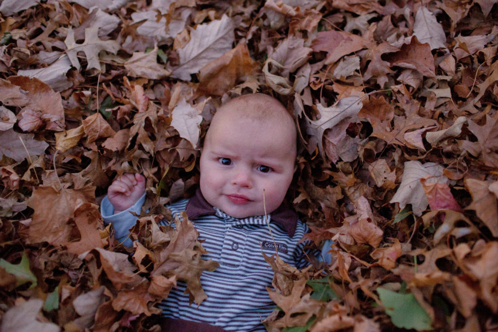 baby boy lays in pile of fall leaves