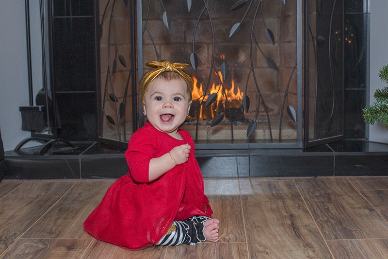 grinning baby sits in front of fireplace
