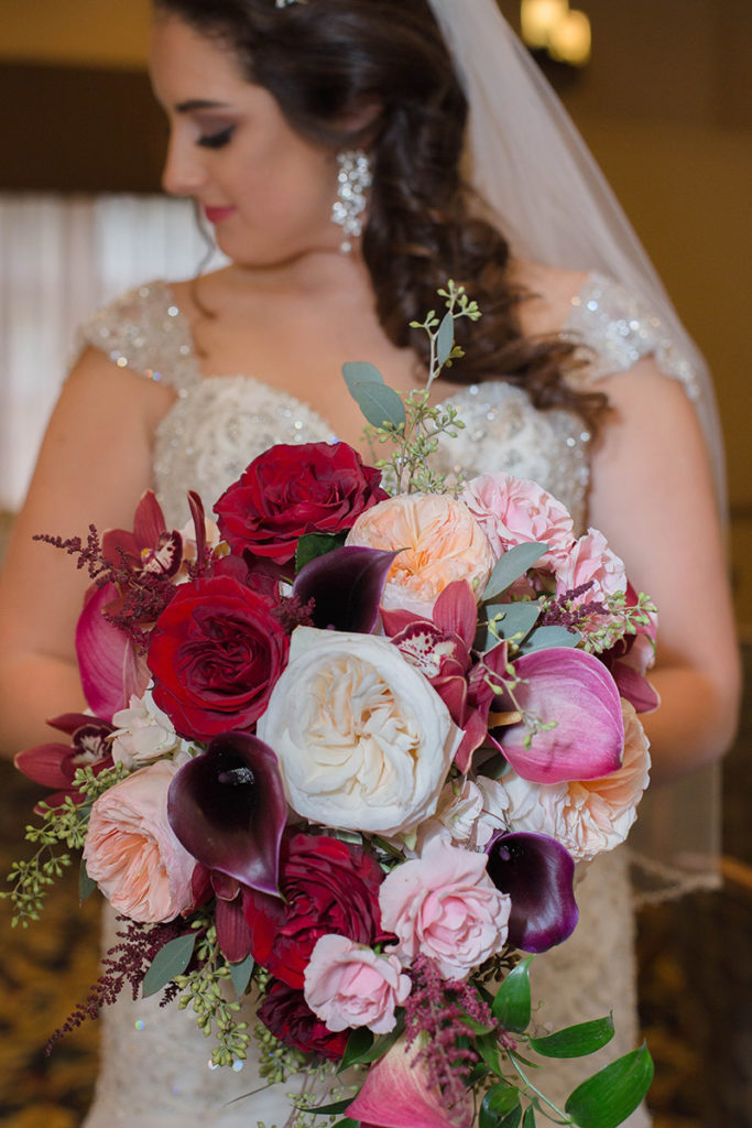bride holds her bouquet of pink, burgundy and white flowers