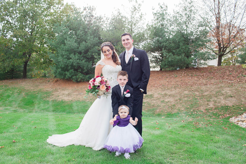 bride and groom stand in yard with their ring bearer and flower girl