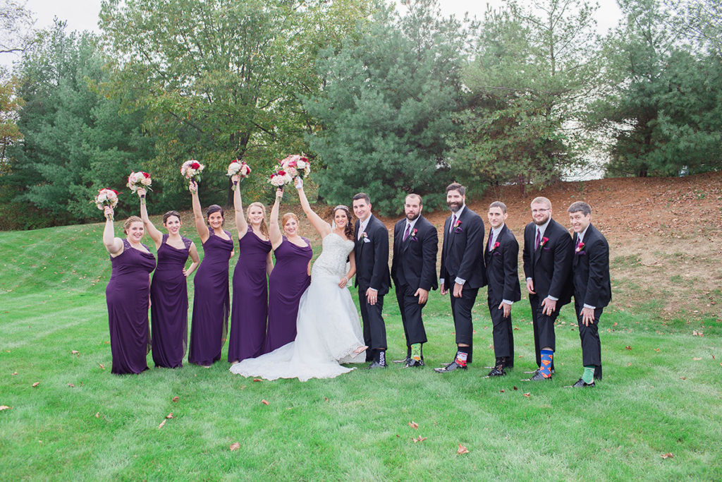 bridal party stand in line, groomsmen showing off their socks and bridesmaids holding their bouquets in the air