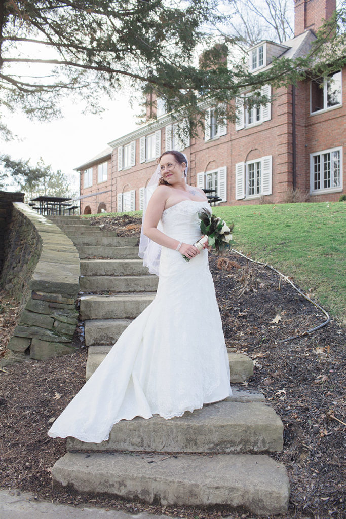 bride stands on stairs in front of mansion at robin hill park