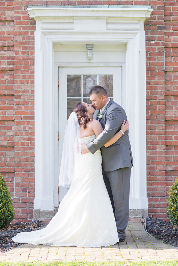 bride and groom stand in front of mansion at robin hill park and kiss