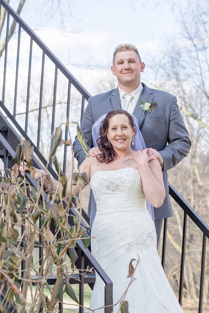 bride and groom stand on iron stairs  outside the mansion at robin hill park