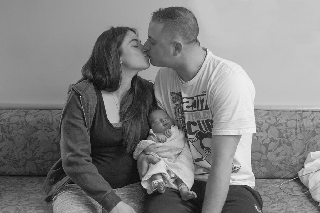 parents kiss while holding new baby 