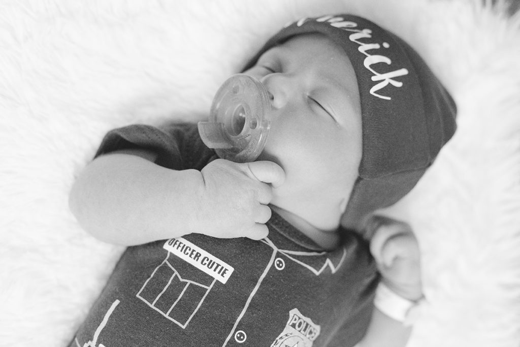 newborn baby wears hat with his name and a police onesie