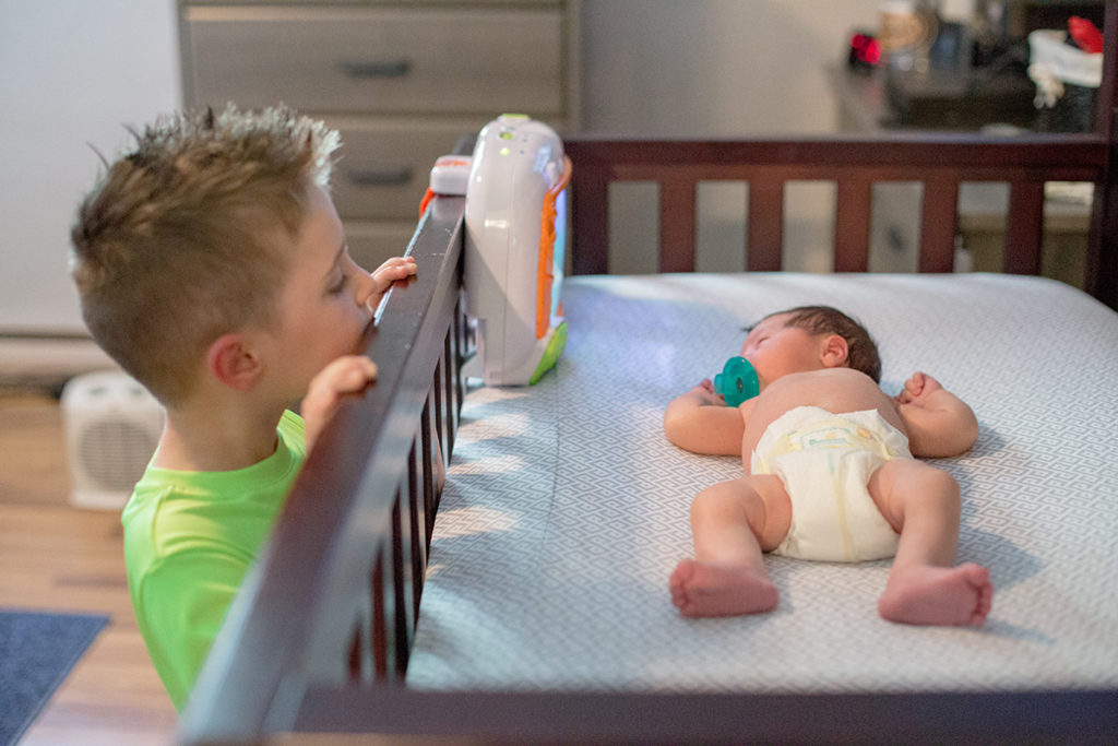 big brother looks over side of crib at his newborn baby brother