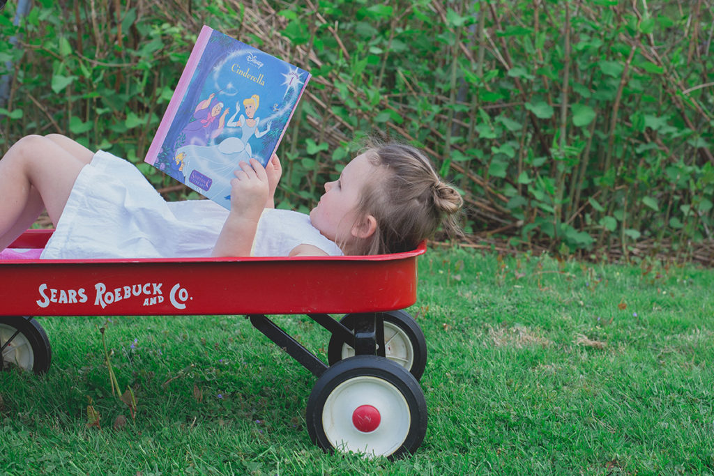 little girl lays in wagon reading a book