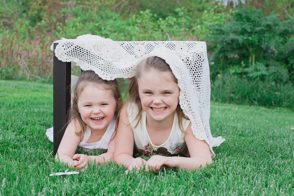 sisters hide under a table with lace table cloth