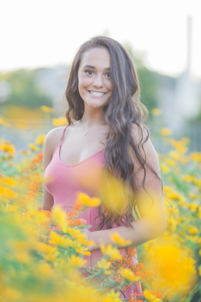 senior girl in pink dress stands among yellow flowers at phipps conservatory