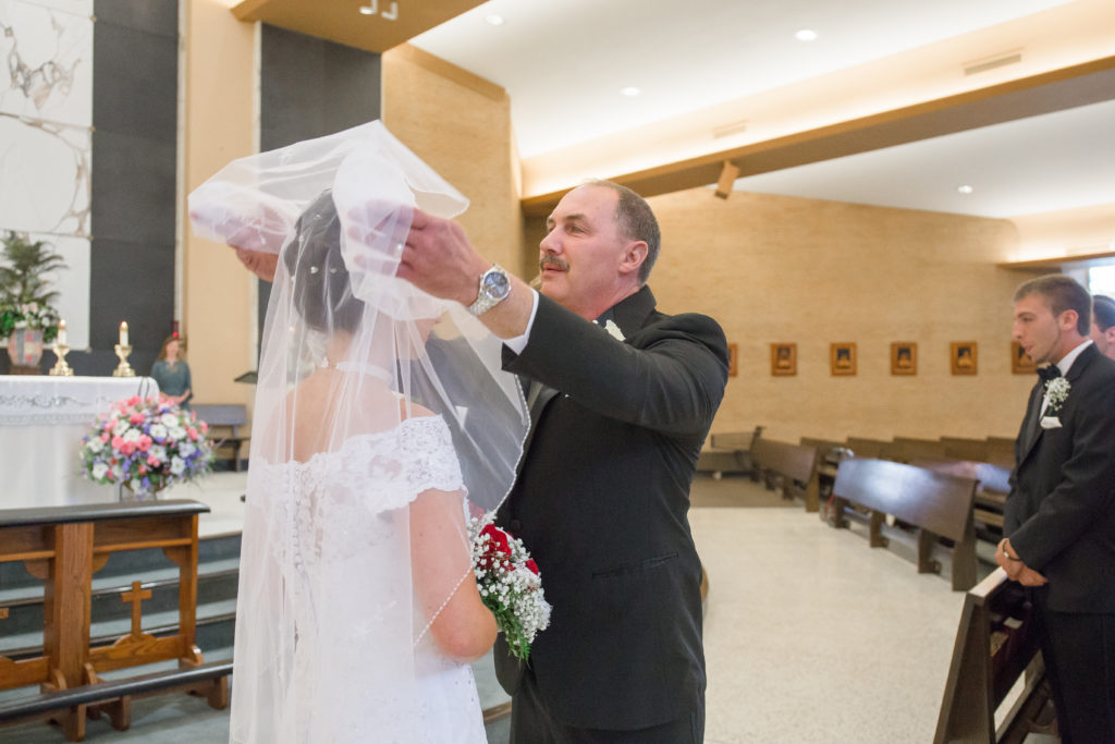 father lifts veil from bride's face as he gives her away