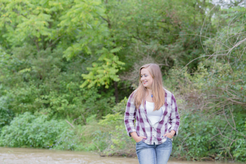 senior girl in flannel and jeans stands in front of creek in milesburg